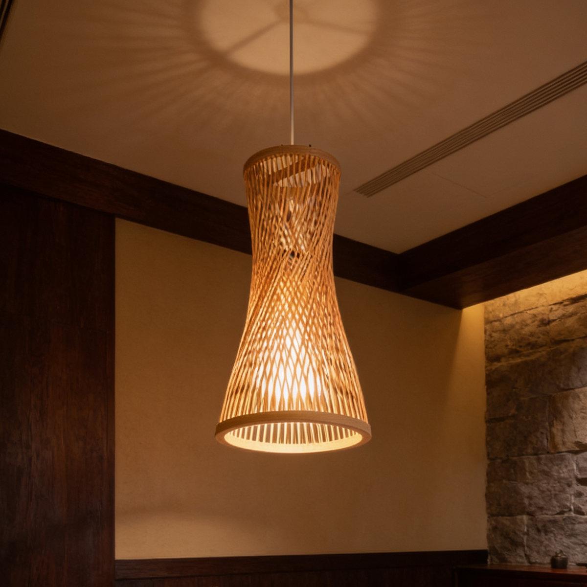 Woven bamboo pendant hanging over a long wooden table by a stone accent wall