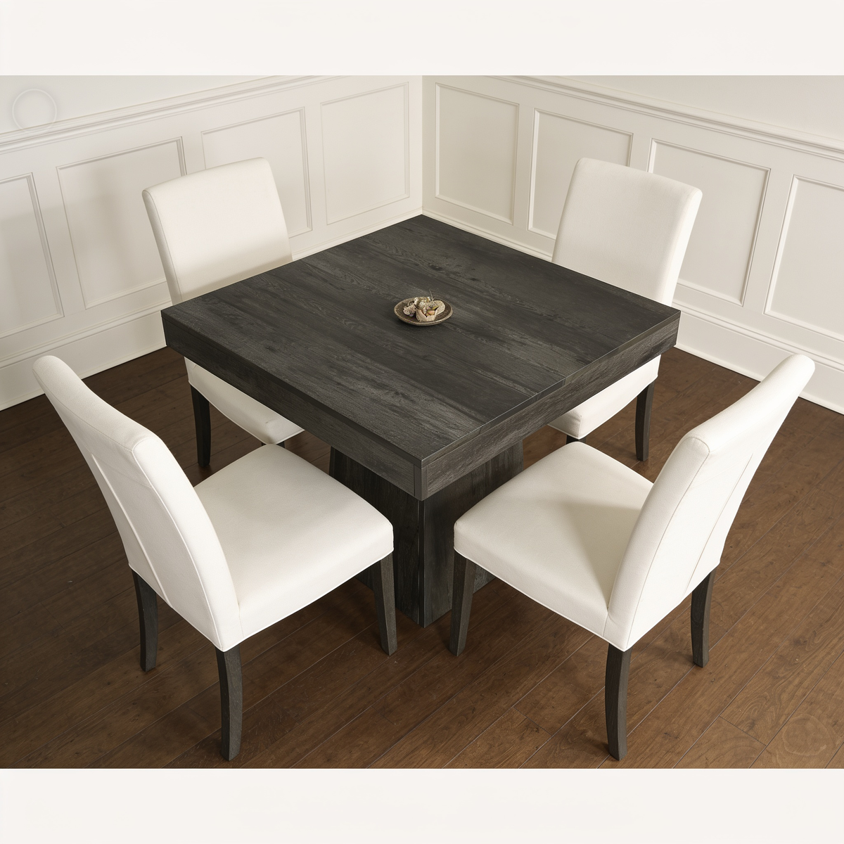 Square gray table with a bowl on top and four cream chairs in a corner nook