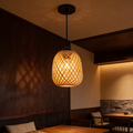 Woven bamboo barrel pendant glowing above a booth seat and dark timber wall
