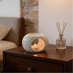 Speckled white ceramic warmer glowing with a tealight beside a reed diffuser