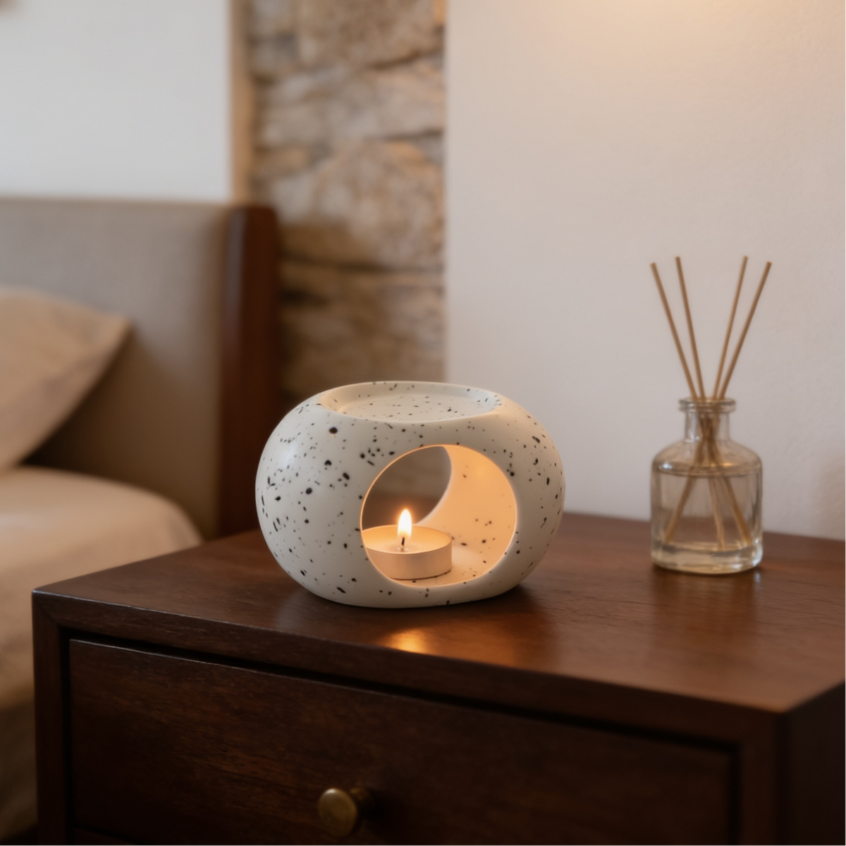 Speckled white ceramic warmer glowing with a tealight beside a reed diffuser
