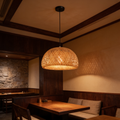 Woven dome pendant lit in front of a stacked stone wall above a dining table