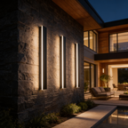 Three slim black LED wall bars washing light down a stone facade at dusk