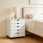 Five drawer cabinet seen from the foot of a bed with a lamp and small plant