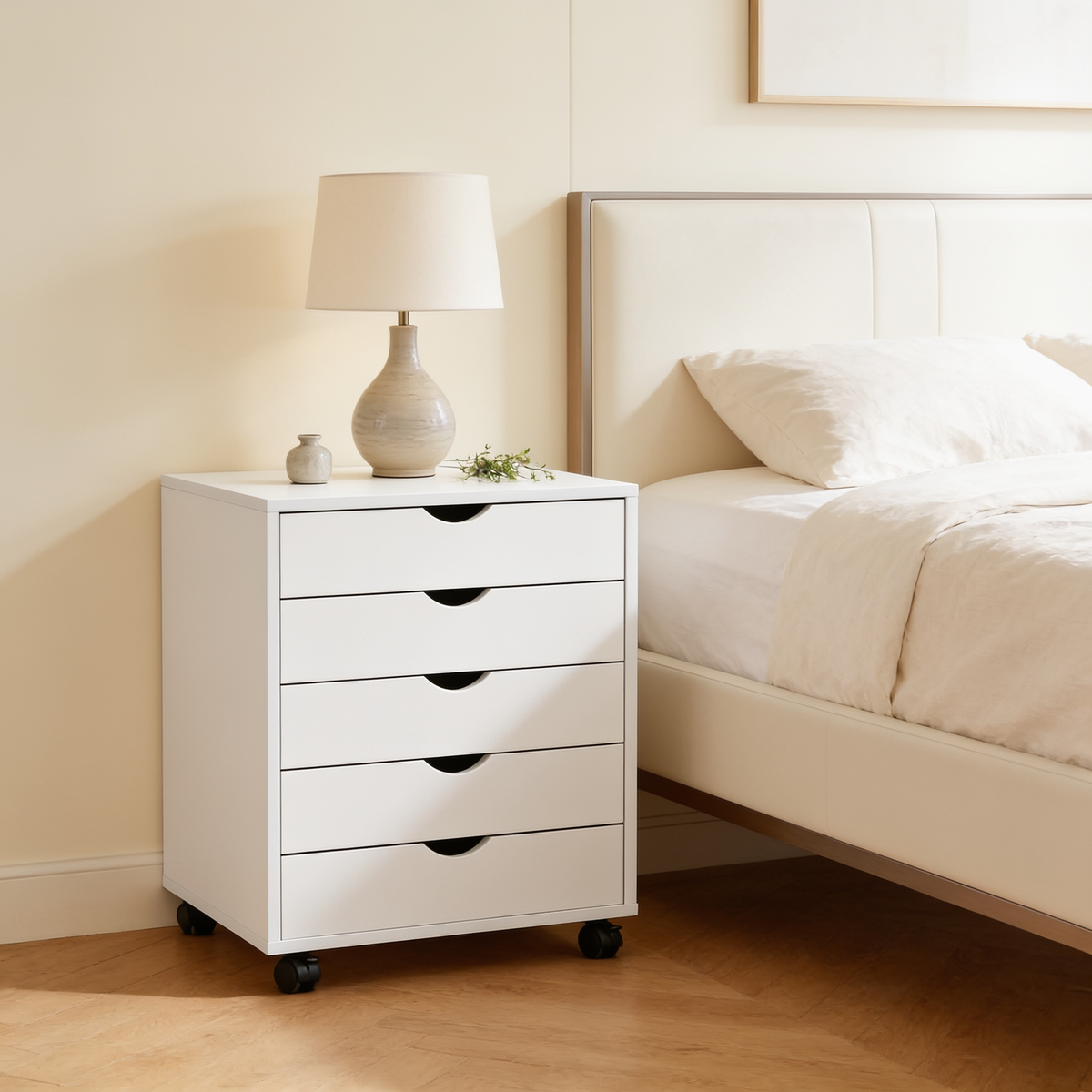 Five drawer cabinet seen from the foot of a bed with a lamp and small plant