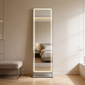Lit full length mirror leaning on a bedroom wall beside an upholstered bench
