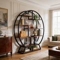 Round black iron bookcase with staggered wood shelves beside a wood sideboard