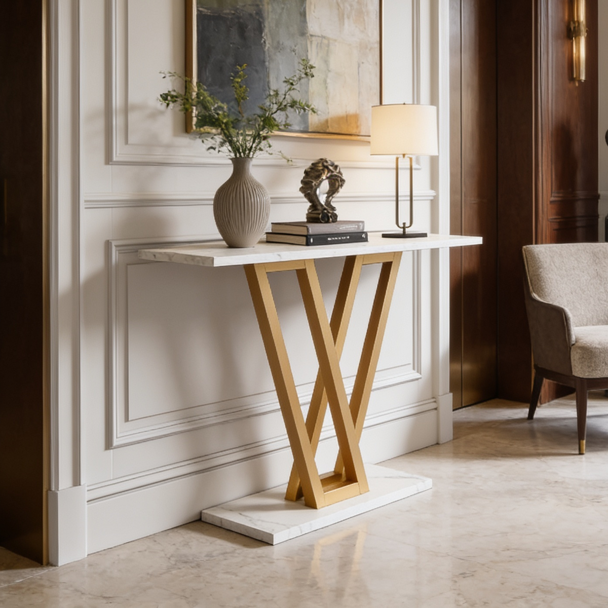 Gold and white entryway console with a table lamp, vase and plant beside chairs