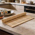 Bamboo rolling mat unrolled on a stone countertop with a plate of sushi behind it