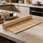 Bamboo rolling mat unrolled on a stone countertop with a plate of sushi behind it