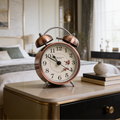 Twin bell alarm clock on a dark nightstand beside a stack of books