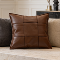 Square brown leather look cushion flanked by gray and cream cushions on a sofa