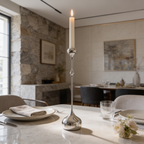 Polished silver teardrop candlestick holding a lit taper on a set dining table