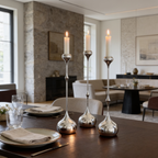 Three silver candlesticks of different heights lit along a dark table