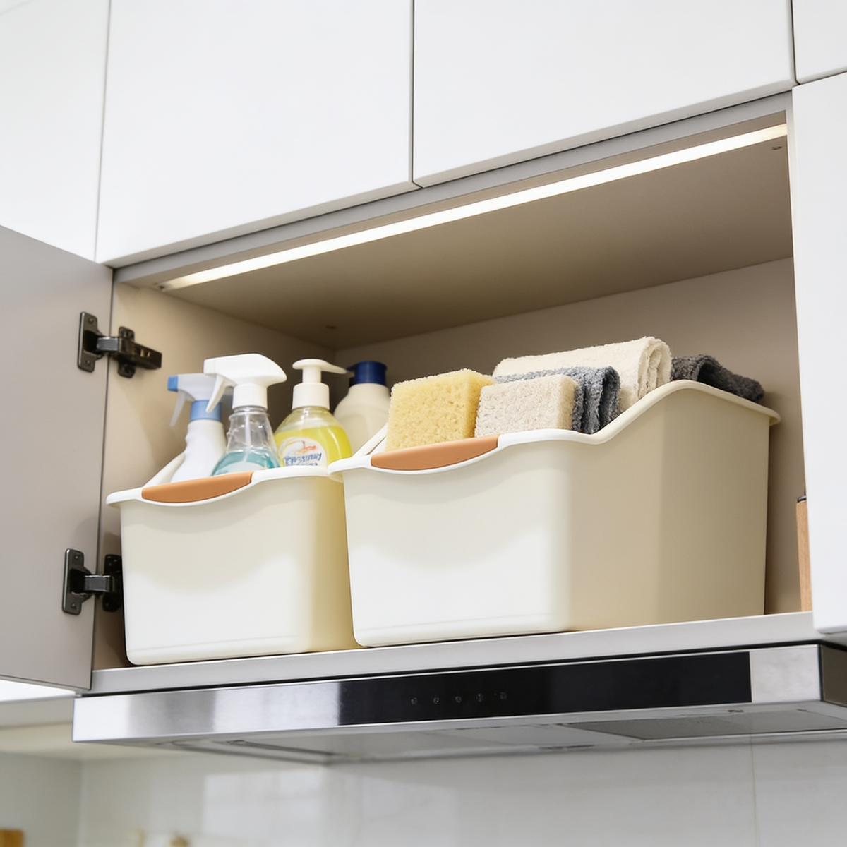 Two cream storage bins with orange grips inside a lit wall cabinet above a stove