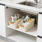 Pair of beige open front bins with orange grips on a white shelf under a stainless sink