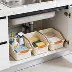 Cream bins with gray grips lined up on a shelf inside an open under sink cabinet