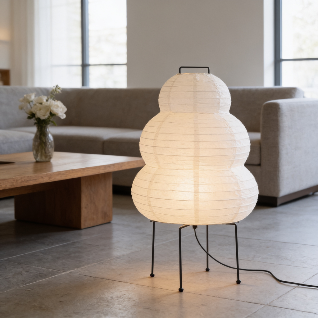 Tiered white rice paper lantern lamp on slim steel legs beside a sofa and wooden table