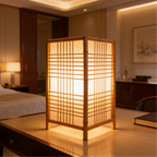 Boxy shoji style lamp lit on a wooden console with a bed in the background