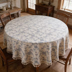 Dense blue toile floral tablecloth with a fringed hem on a round farmhouse table