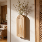 Wall mounted wood vase with tall dried branches beside a slim mirror