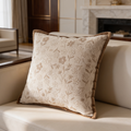 Pale beige cushion with a scattered flower weave and rope trim seen beside a fireplace