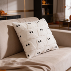 Cream ghost face pillow propped at an angle on a sofa beside a fireplace