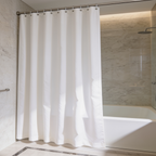 Plain white bath curtain gathered beside a bathtub against a warm marble wall