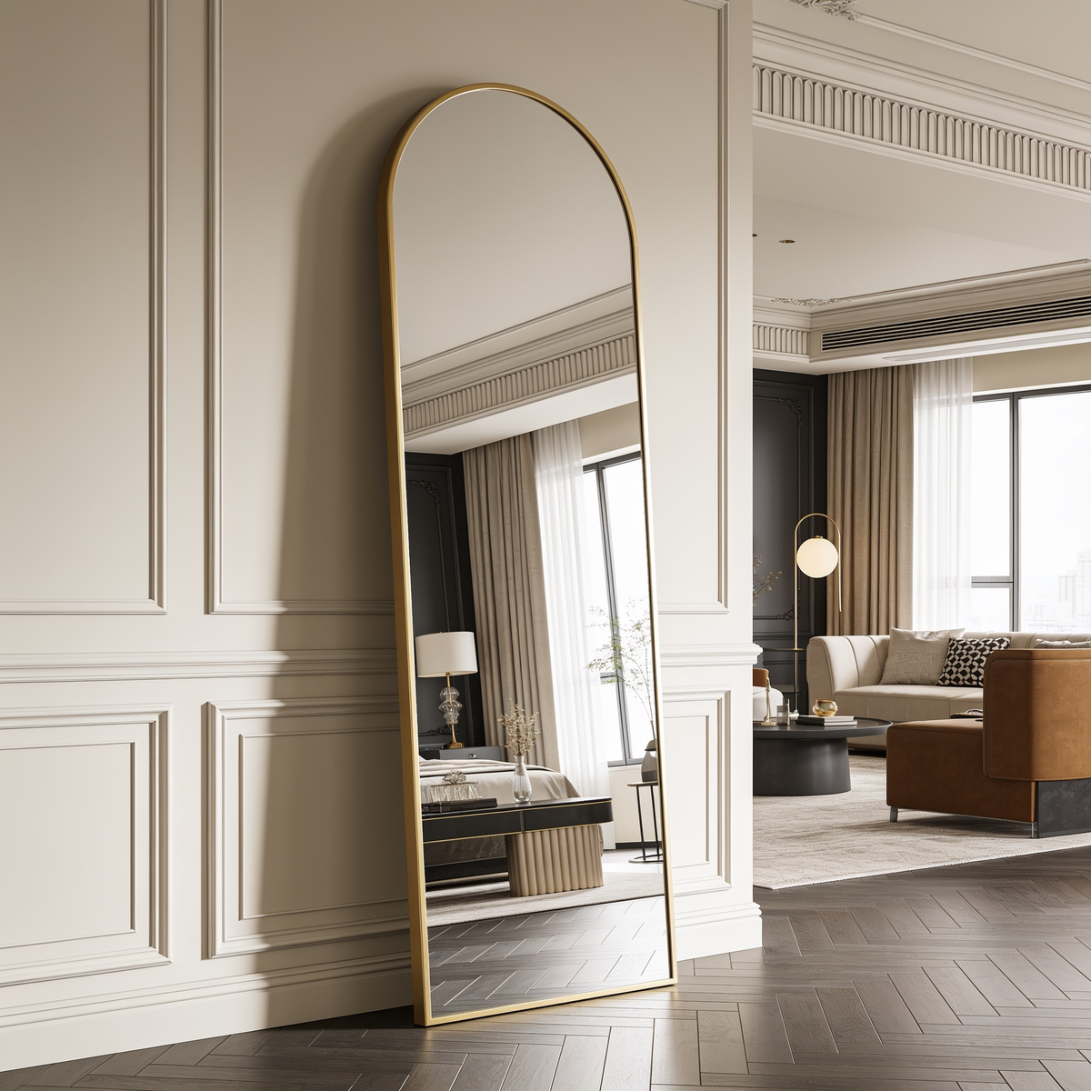 Arched brass framed mirror leaning in a paneled room, reflecting a window and sofa