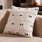 Cream plush pillow cover quilted with ghost faces resting on a light sofa