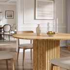 Light oak round table on a fluted cylinder pedestal below framed wall art