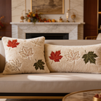 Two maple leaf embroidered pillows on a sofa in front of a marble fireplace