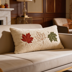 Cream lumbar pillow stitched with three maple leaves resting on a pale sofa