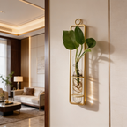 Gold framed tube with a leafy cutting on a cream wall by a lamp