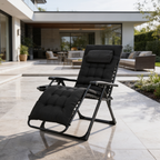 Black cushioned recliner on a stone patio with outdoor lounge seating behind