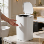 Hand waving above the white sensor trash can to open its lid beside a bathtub
