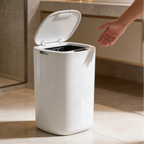 White sensor trash can with the lid open showing a black liner on a bathroom floor