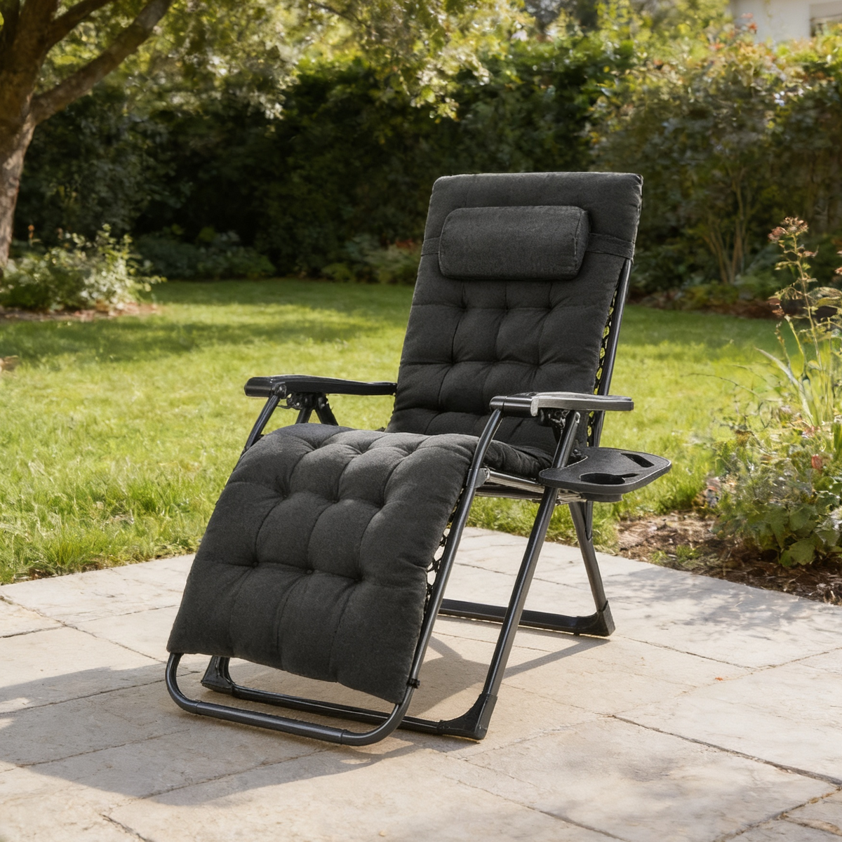 Black cushioned recliner angled on a patio in front of a clipped hedge and tall trees