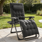 Black padded zero gravity recliner on a stone patio with its swing out tray and a lawn behind