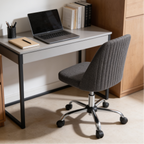 Gray armless swivel chair rolled up to a white desk with a laptop and a stack of books