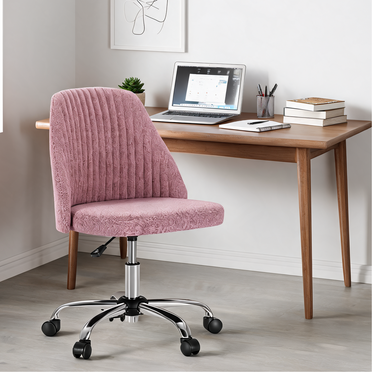 Pink armless chair at a wooden desk with a laptop, books and a potted plant
