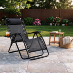 Black zero gravity chair reclined beside a lawn with a tall iced tea on the cup holder tray