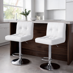 White stools facing a dark island in a bright kitchen with cabinets and a tall window