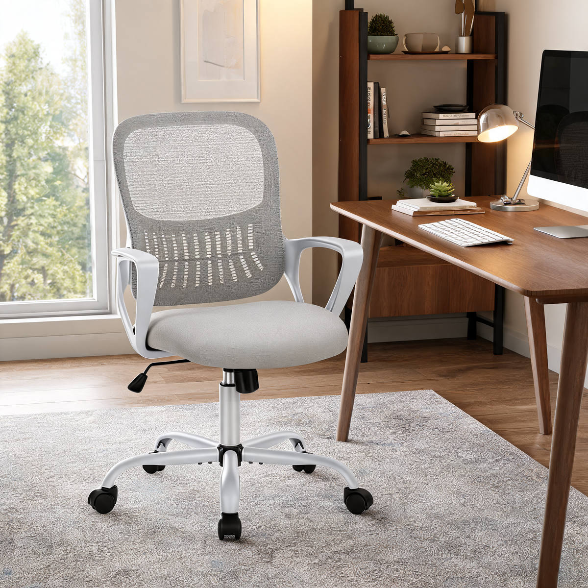 Gray mesh task chair with flip up arms beside a bright window and a wood desk with a keyboard