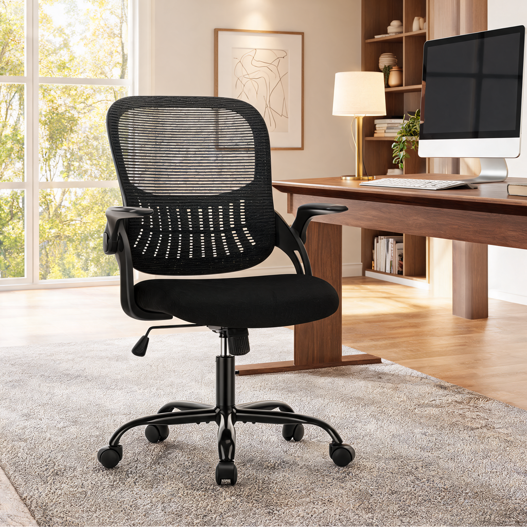 Black mesh office chair on a shaggy rug in front of a window and a wooden desk with a monitor