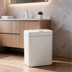 Closed white sensor trash can beside a wood vanity holding a plant and soap