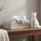 Two white geometric cat figures on a wood table, one resting on a stack of books